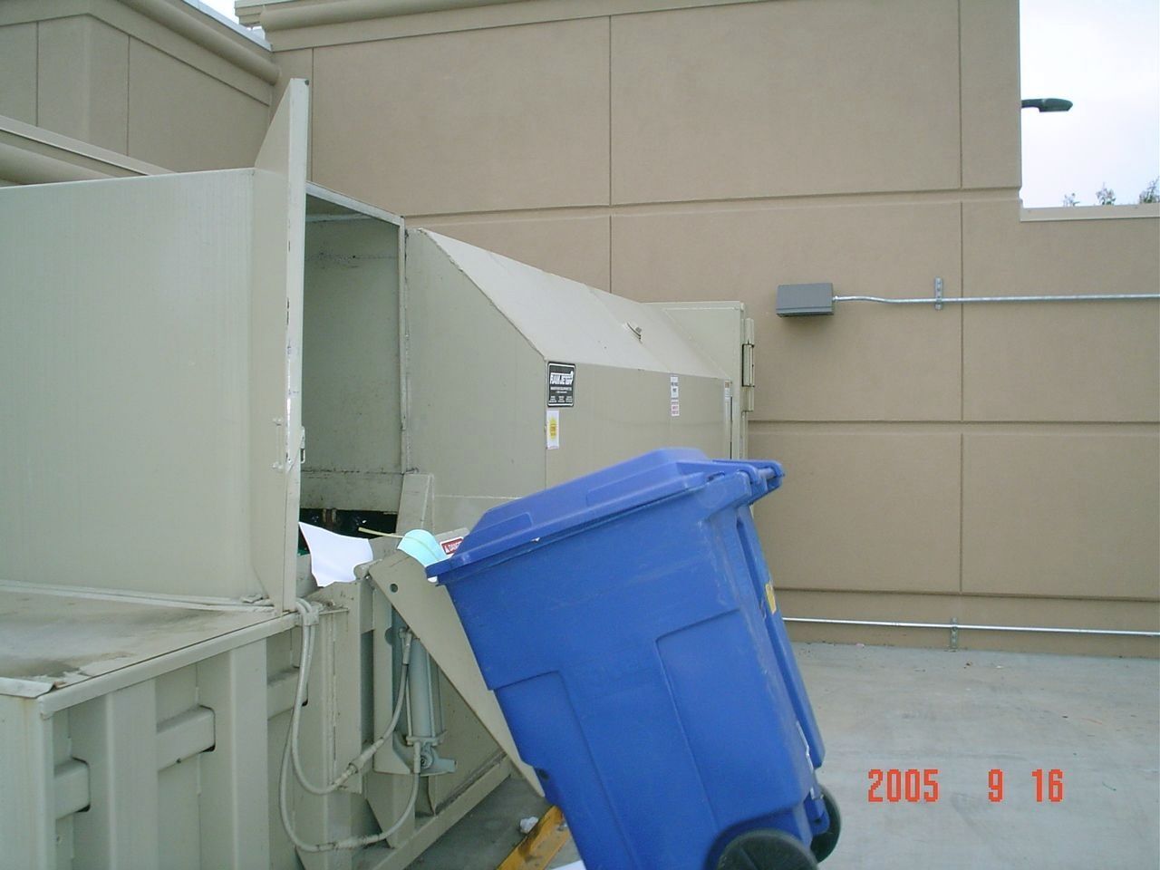 ACES trash compactor installed beside a building with a rolling toter cart